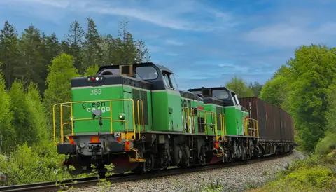 Diesellok drar vagnar i vacker natur.